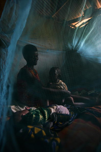 A mother and her child in Africa sit under a bed net that can help prevent malaria. 