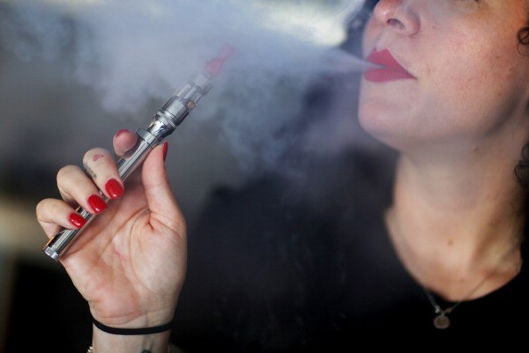 A woman using an e-cigarette, blowing out the vapor that contains nicotine.
