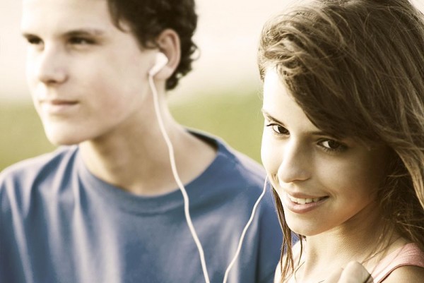 Teens sharing earphones, listening music outdoor. Summer time.